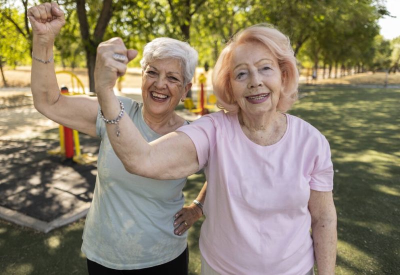 stock-photo-two-elderly-female-friends-enjoying-time-outdoor-park-gym-flexing
